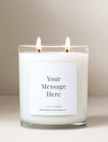 Two-wick scented candle in a clear glass jar with a customizable white label on a neutral background. - Image 