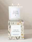 Two-wick scented candle in a glass jar with a personalized label, resting on a patterned gift box with botanical designs. - Image 
