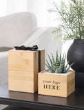 Two light natural wood gift boxes on a dark table, with one stacked box tied by a black ribbon and one open box containing a small striped succulent. The front box has the text 'your logo HERE'. - Image 