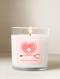 Lit candle in a clear glass jar with a pink label featuring a heart, stethoscope, and Everyday Heroes text. - Image 