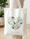 White cotton tote bag with a floral heart design of green leaves and purple flowers, personalized with "LULA'S GARDEN". - Image 